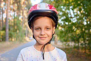 Kaskını takmış gülümseyen ve yaz tatilinde paten kaymaya ya da bisiklete binmeye hazır gülümseyen kız çocuğunun portresi.