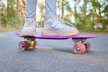 Bilinmeyen çocuğun bacakları mor kaykayın üzerinde tanınmaz halde genç bayan kaykaycı dinlenme ve yaz sporlarının tadını çıkarıyor.