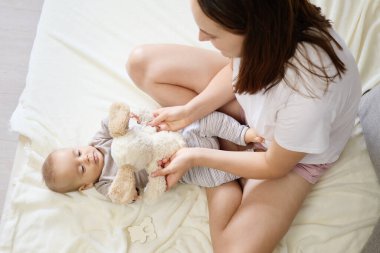 Anne ve küçük oğlu tüylü oyuncaklarını tutuyorlar ve evlerinin sıcaklığında gülümsüyorlar. Yatakta oturmuş, birbirlerine bağlanıyorlar. Sessiz ve huzurlu bir yuvada bebekliğin eğlenceli anlarının tadını çıkarıyorlar.