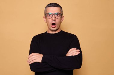 Kafkasyalı erkek, bej arka planda kapalı bir şekilde bekleyerek inanılmaz çığlıklar attığını duyunca ağzı açık kalmış, ağzı açık kalmış, şok olmuş.