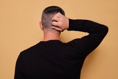 Düşünceli bir adam, kazağını giyer arkasını dönüp bakarken başını ovuşturur. Bej arka planda kapalı bir yerde duran bir şeyi düşünmekten rahatsız olur.