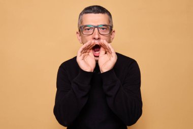 Gözlük takan, siyah hareketler yapan, yüksek sesle bağıran, önemli bilgileri bej arka planda izole edilmiş katı bir ifadeyle sunan, kendinden emin bir adam.