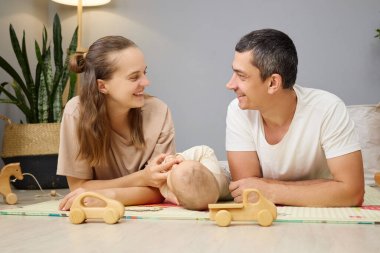 Sevimli bir çift anne ve baba yerde yatar ve yeni doğmuş bebeklerle birbirlerini seyrederler. Nazik bir gülümsemeyle, şefkatli ebeveynlik ve aile bağlarının keyfini çıkarırlar.