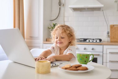 Küçük kız dizüstü bilgisayarıyla mutfakta oturmuş çizgi film izliyor internette geziniyor ve çocuk oyunları oynuyor. Dijital zamanının tadını çıkarıyor ve evde ders çalışıyor.