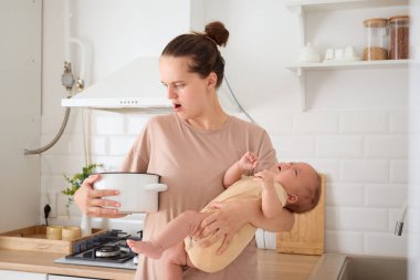 Şok olmuş bir kadın, mutfakta bebeğiyle, çömlekteki bozuk yemekleri keşfederken ve bebeğini kucağında tutarken ve ev hanımı olarak sorumluluklarını dengelemeye çalışırken şoka girdi.