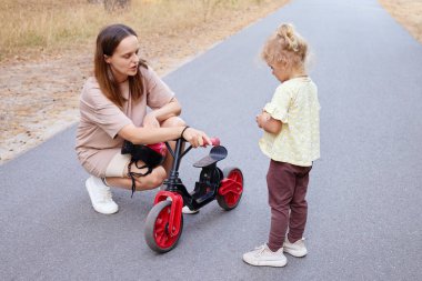 Yürüyen kız annesiyle bisiklete binmeye çalışıyor. Ona yardım ediyor ve dengeli bisikleti nasıl kullanacağını anlatıyor.