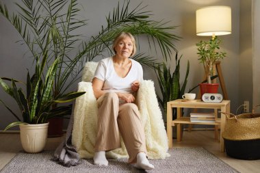 Sakin, kıdemli bir kadın evdeki koltuğunda dinleniyor. Oturma odasında mutlu ve mutlu hissediyor. Huzurlu bir şekilde emekliliğinin tadını çıkarıyor.