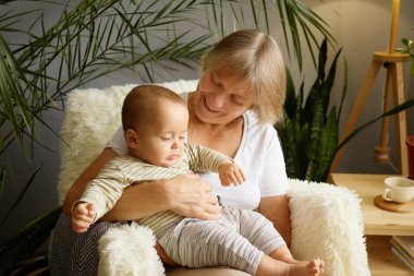 Huzurlu yaşlı kadın emekli evinde rahat koltuğunda küçük torunuyla oynuyor sevgi ve mutlulukla dolu emeklilik yıllarının tadını çıkarıyor.