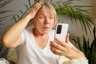 Son sınıf öğrencisi kadın şok olmuş bir ifadeyle akıllı telefondan internete girip sosyal medyayı karıştırıyor ve evdeki alışveriş uygulamasından gelen ani uyarıyı fark ediyor.