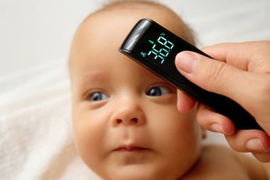 Tanımlanamayan anne hasta yeni doğan oğlunun ateşini dijital termometreyle ölçüyor.