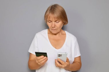 Üst düzey kadın, bankacılık uygulaması ve gri arkaplana karşı işlem yaparken cep telefonu kullanarak çevrimiçi alışveriş için kredi kartı verilerine ciddi şekilde odaklandı