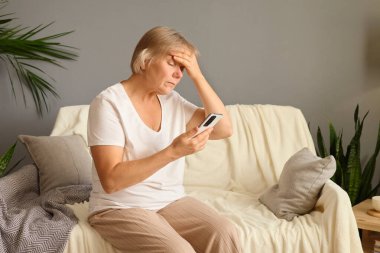 Sağlıksız, olgun bir kadın cep telefonuna sarılıp evdeki kanepede oturan virüs yüzünden baş ağrısı ve yüksek ateşi olan doktorla çevrimiçi konsültasyon arıyor.
