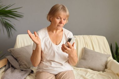 Yaşlı, belirsiz bir kadın evinde kanepede şaşkın şaşkın oturuyor. Cep telefonuyla çevrimiçi kayarken ve emekliliğinde teknoloji kullanırken internetteki şok edici içeriği görüyor.
