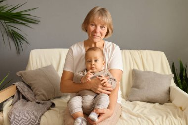 Mutlu gülümseyen büyükanne ve torun, evde kanepede oturup, aile eğlencelerinin tadını çıkararak ev içinde rahat bir şekilde vakit geçiriyorlar.