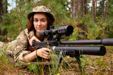 Askeri kıyafetli yetenekli bir nişancı sabahın erken saatlerinde yemyeşil bir ormanda keskin nişancı tüfeğini hedef alırken dikkatle odaklanır..
