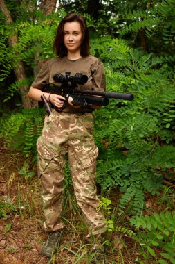 A soldier poses in a military-style outfit, holding a sniper rifle while surrounded by dense green foliage, showcasing a sense of readiness and focus in nature. clipart