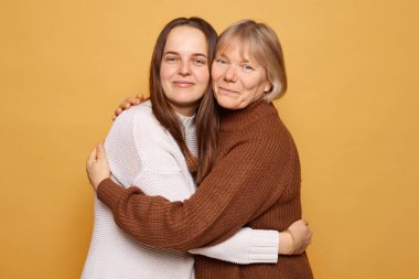 Parlak sarı bir geçmişi olan neşeli bir ortamda, iki kadın, güçlü ilişkilerini ve mutluluklarını sembolize eden, samimi bir kucaklaşmayla sevgiyi ve bağlantıyı ifade eder..