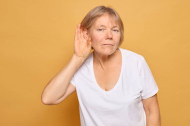 Kısa sarı saçlı bir kadın aktif olarak dinliyor, eli kulağına yapışık, birinin canlı sarı bir fon hakkında ne söylediğiyle ilgili merakını ya da ilgisini gösteriyor..