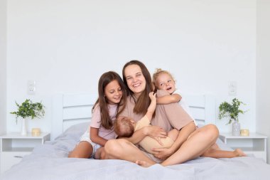 Bir anne, aydınlık bir yatak odasında üç çocuğuyla neşeli anlar paylaşır. Gülüp gülüyorlar, birlikte sıcak ve sevgi dolu bir ortam yaratıyorlar..