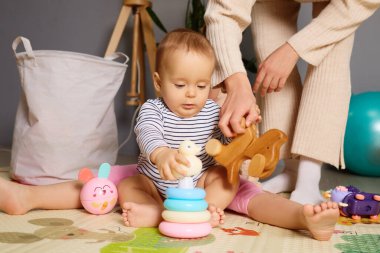 Bir bebek renkli istifleme halkaları ve tahta bir oyuncak hayvanla meşgul olur. Dekor, yumuşak ışıklandırmayla sıcak bir iç mekan ve rahat bir atmosfer sağlıyor..