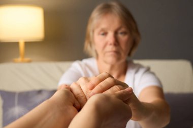 Yaşlı bir kadın el ele tutuşmaya çalışır, dingin, hafif aydınlatılmış kapalı bir ortamda, duygusal refahı destekleyen bir bağlantı ve destek duygusu yaratmaya odaklanır..