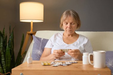 Son sınıf öğrencisi bir kadın evdeki ilaç paketlerini inceliyor. Etrafı rahat bir oturma odası ile çevrili. Doğal ışık boşluğu doldurur. Odaklanıp düşüncelere dalarken..