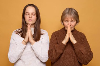 Birinde uzun saçlı, diğerinde kısa gri saçlı iki kadın, gözleri kapalı ve elleri sıcacık sarı bir zemin üzerinde meditasyon pozu vererek birbirlerine yakın dururlar..