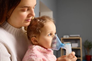 A mother calmly assists her young daughter with an inhaler, providing respiratory treatment in a warm and inviting room. The atmosphere feels nurturing and supportive. clipart