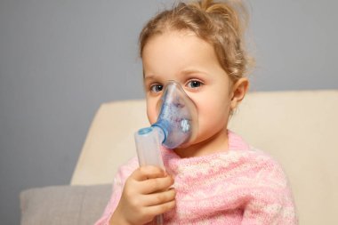 Genç bir çocuk nebulizör maskesiyle rahat bir şekilde oturuyor ve solunum tedavisi görüyor. Yumuşak ışık odada rahatlatıcı bir atmosfer yaratır..