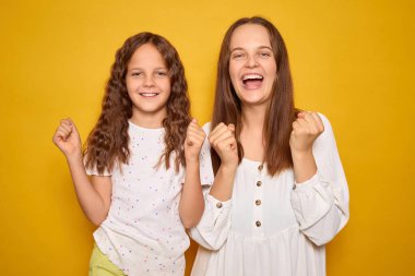 Bir anne ve kız yan yana durur, yumruklarıyla gülümseyerek mutlu bir anı kutlarlar. Onların neşeli ifadeleri sahneye sıcaklık getirir..