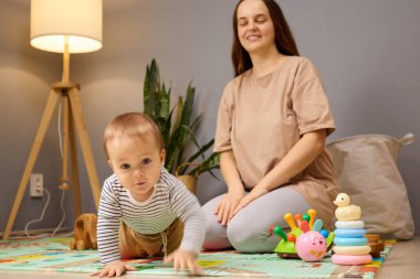 Parlak bir kapalı alanda, genç bir çocuk canlı bir oyun hasırının üzerinde emekler, oyuncaklarla mutlu mesut meşgul olurken, gülümseyen bir anne yakınlarda sevgiyle izler. Sıcak ışık davetkar atmosfere ekleniyor..