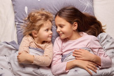 İki genç kız kardeş, yumuşak bir yatakta yan yana uzanıp, gece boyunca yatak odalarındaki battaniyenin altına kıvrılıp, gülüşlerini ve gülüşlerini paylaşıyorlar..