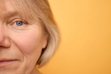 A woman with light blonde hair is smiling gently against a bright yellow backdrop. Her expression conveys warmth and kindness as she engages the viewer. clipart