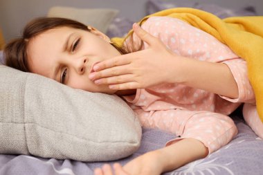 Bir kız yatağa uzanmış, yorgun ve hasta görünüyor, üzerinde sarı bir battaniye var. Esnerken başını yastığa koyar. Bu da yeni uyandığını gösterir..