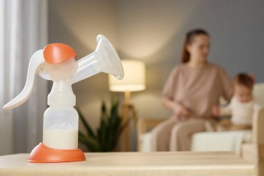 Bir anne bebeğiyle etkileşime girerken bir anne, yumuşak bir şekilde aydınlatılmış bir oturma odasındaki bir masada oturur ve birbirlerine bağlanmaları için besleyici bir ortam sağlar..