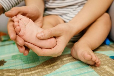 Her ikisi de renkli bir oyun hasırının üzerinde oturan bir çocuğun ayağına masaj yapan bir yetişkin gibi nazik bir etkileşim meydana gelir. Bu besleyici an, neşeli bir kapalı mekan aktivitesi sırasında sevgi ve bağın altını çiziyor..