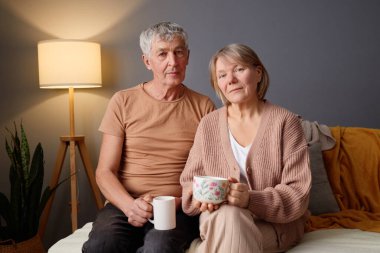 Olgun bir çift sıcak tonlu bir odada koltukta rahatça oturup içkilerini yudumluyor..