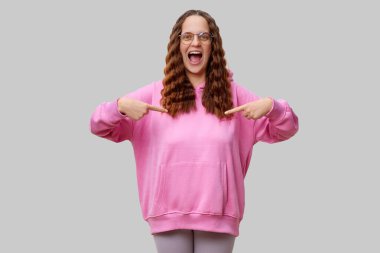 Kıvırcık saçlı, gözlüklü, pembe kapüşonlu bir kadın. Büyük bir tebessümle kendini gösteriyor, heyecanını ve özgüvenini açıkça ifade ediyor..