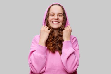 Pembe kapüşonlu uzun kıvırcık saçlı bir kadın kumaşı şakacı bir şekilde çekerken sıcak bir şekilde gülümsüyor. Neşeli tavırları, tarafsız bir ortamda mutluluk ve rahatlık yayıyor..