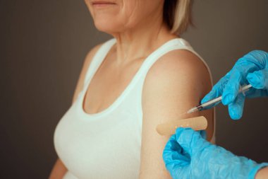 A healthcare worker in gloves administers a vaccination to a woman with short hair. The woman has a bandage on her upper arm and appears calm during the inoculation process. clipart