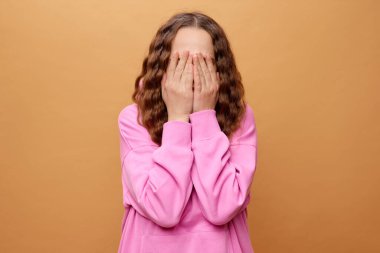 Genç bir birey sırtı kameraya dönük durur, yüzünü iki eliyle saklar..