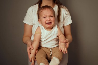 Sıkıntılı bir bebek bir yetişkinin kucağında oturup ağlama belirtileri gösterir. Yetişkin, bebeği nazikçe minimalist bir iç mekanda tutarak sıcaklık ve bağlantı hissi yaratıyor..
