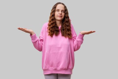 Pembe büyük kapüşonlu genç bir adam sorgulama jestinde kaldırılan ellerle şaşırmış görünüyor. Arkaplan basit bir gri renktir, karmaşanın ifadesini geliştirir..