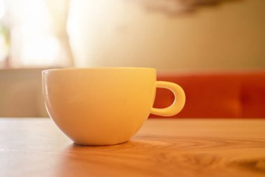 Seramik bir bardak yumuşak öğleden sonra ışığıyla aydınlatılmış pürüzsüz bir ahşap masanın üzerinde duruyor. Sıcak ortam içeceklerden ve rahatlıktan zevk almak için mükemmel bir yer..