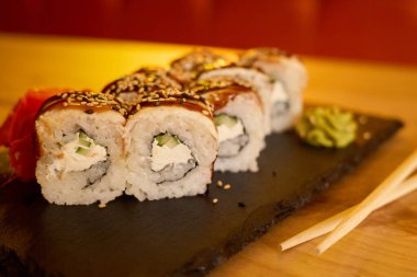 Üzerine tatlı bir jöle sürülmüş suşi ruloları siyah bir taş tabakta sunulur. Eşlik eden wasabi ve turşulu zencefil sıcak bir yemek atmosferinde yemeğe canlı bir renk katar..