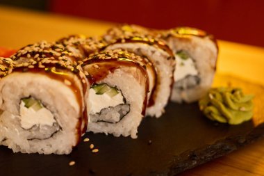 Nefis suşi ruloları siyah bir tabakta sunuluyor, sosla güzelce serpilmiş ve susam tohumlarıyla süslenmiş. Canlı wasabi bu gurme yemeğini tamamlıyor..