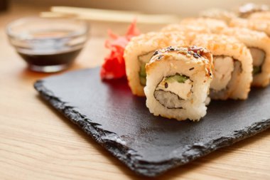 Taze balık ve sebzelerle dolu lezzetli suşi ruloları bir tabakta sunulur. Soya sosu ve turşulu zencefil yemeğin tadını artırır..