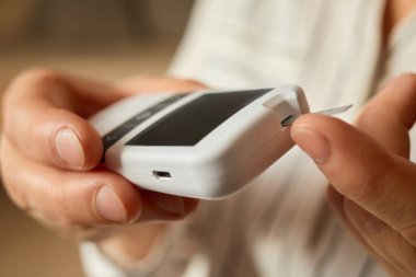 Biri glikoz seviyesini ölçmek için glukometreye test bandı yerleştiriyor. Bu etkinlik, diyabetin düzenli olarak izlenmesi ve sağlığın korunmasının önemini vurgulayarak kapalı alanlarda gerçekleşir..