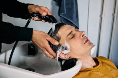 Bir adam yeni bir saç kesimine hazırlanırken berber dükkanında dinlendirici bir saç yıkamanın keyfini çıkarıyor. Kuaför dikkatlice şampuanını sürüyor ve saçını duruluyor, rahatlatıcı bir atmosfer yaratıyor..