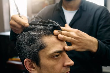 Yetenekli bir kuaför, yoğun bir öğleden sonra bir berber dükkanında müşterisine titiz bir saç kesimi yapmaya odaklanır. Kuaför makas ve tarak kullanır..